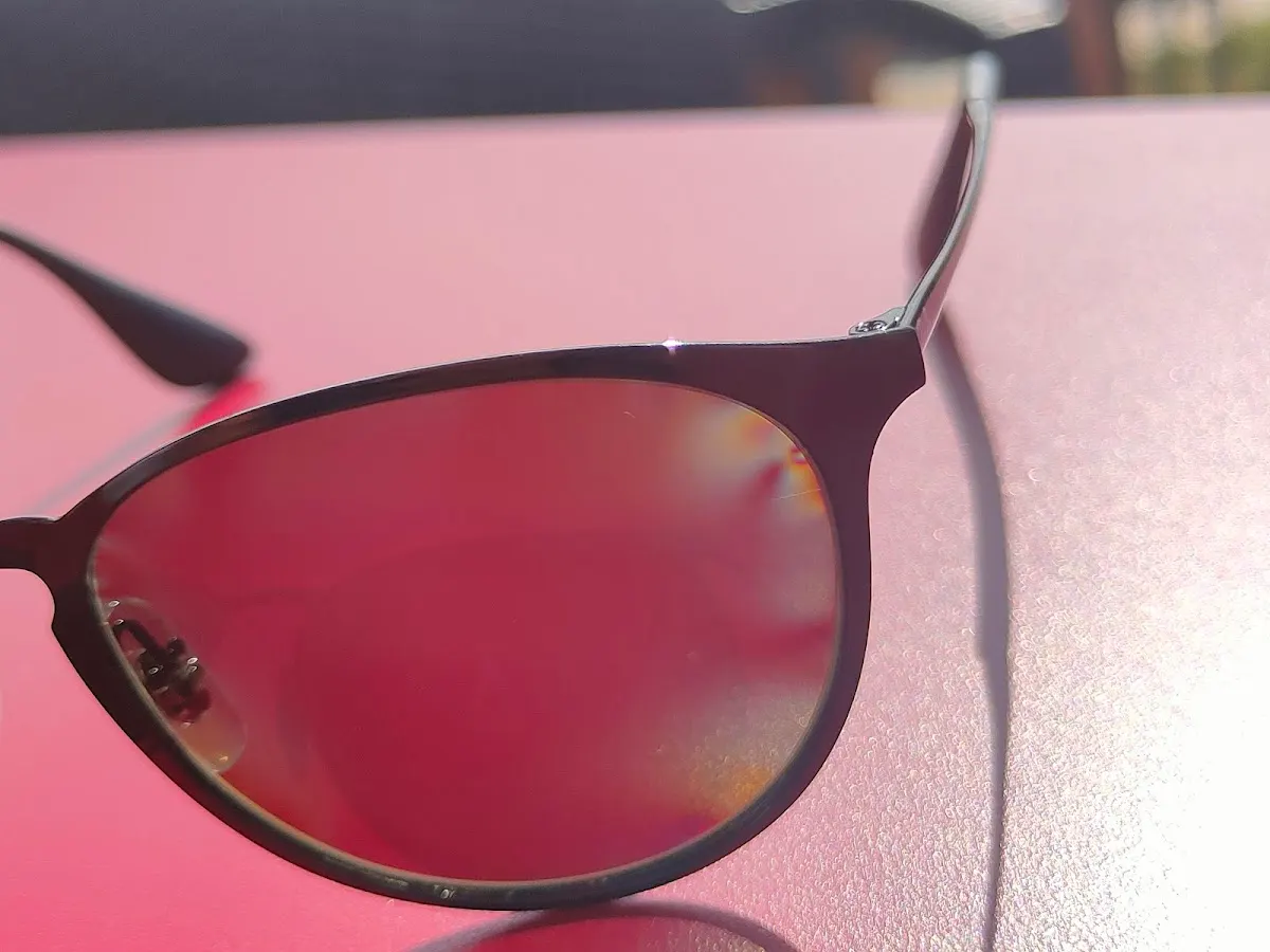 Detalle de unas gafas de sol de montura oscura y lentes rojizas.
