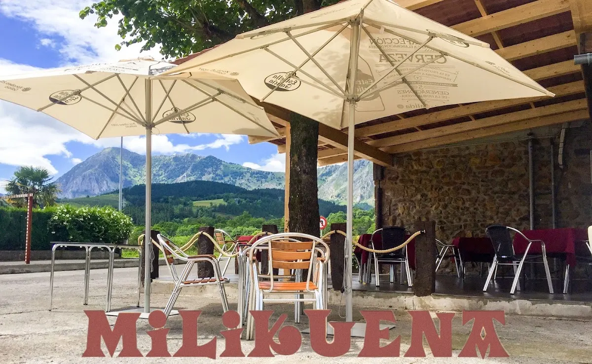 Terraza exterior de Milikuena Jatetxea con mesas, sombrillas y vistas al monte.