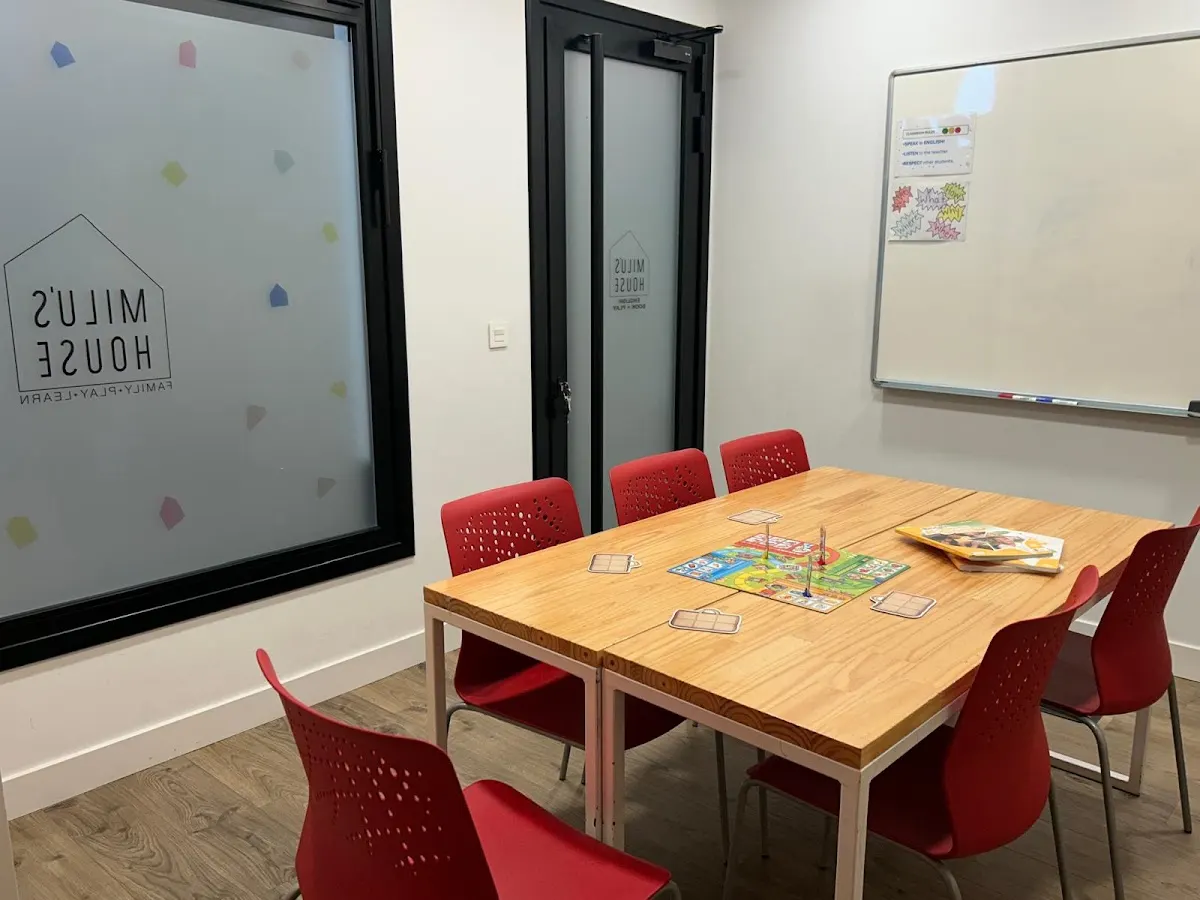 Aula de Milu's House con mesa, sillas rojas y pizarra