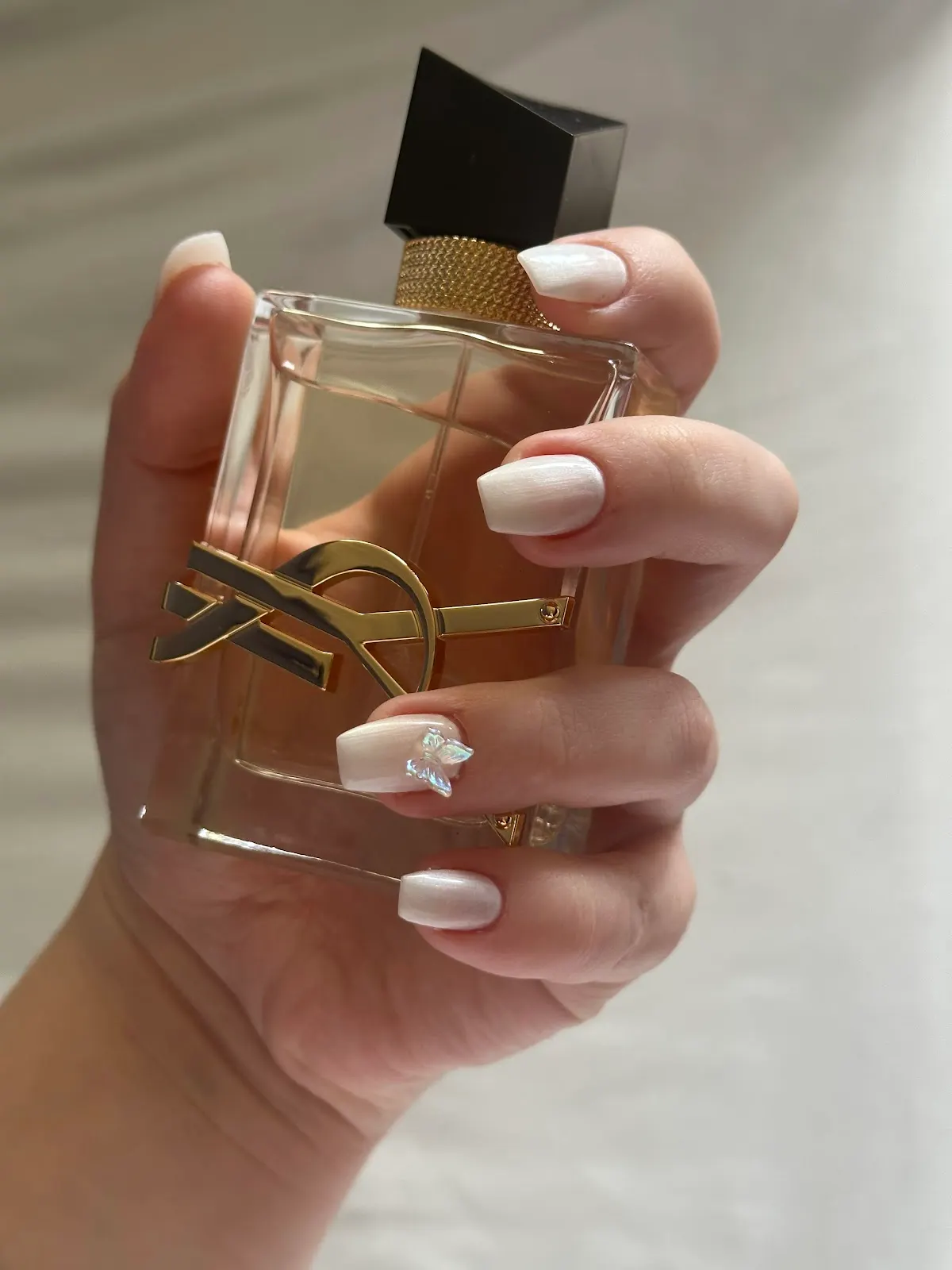 Manicura blanca con detalle decorativo junto a un frasco de perfume