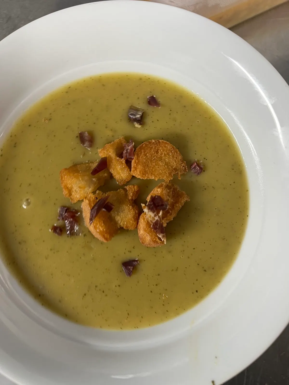 Crema servida en un plato hondo con picatostes y taquitos de jamón.