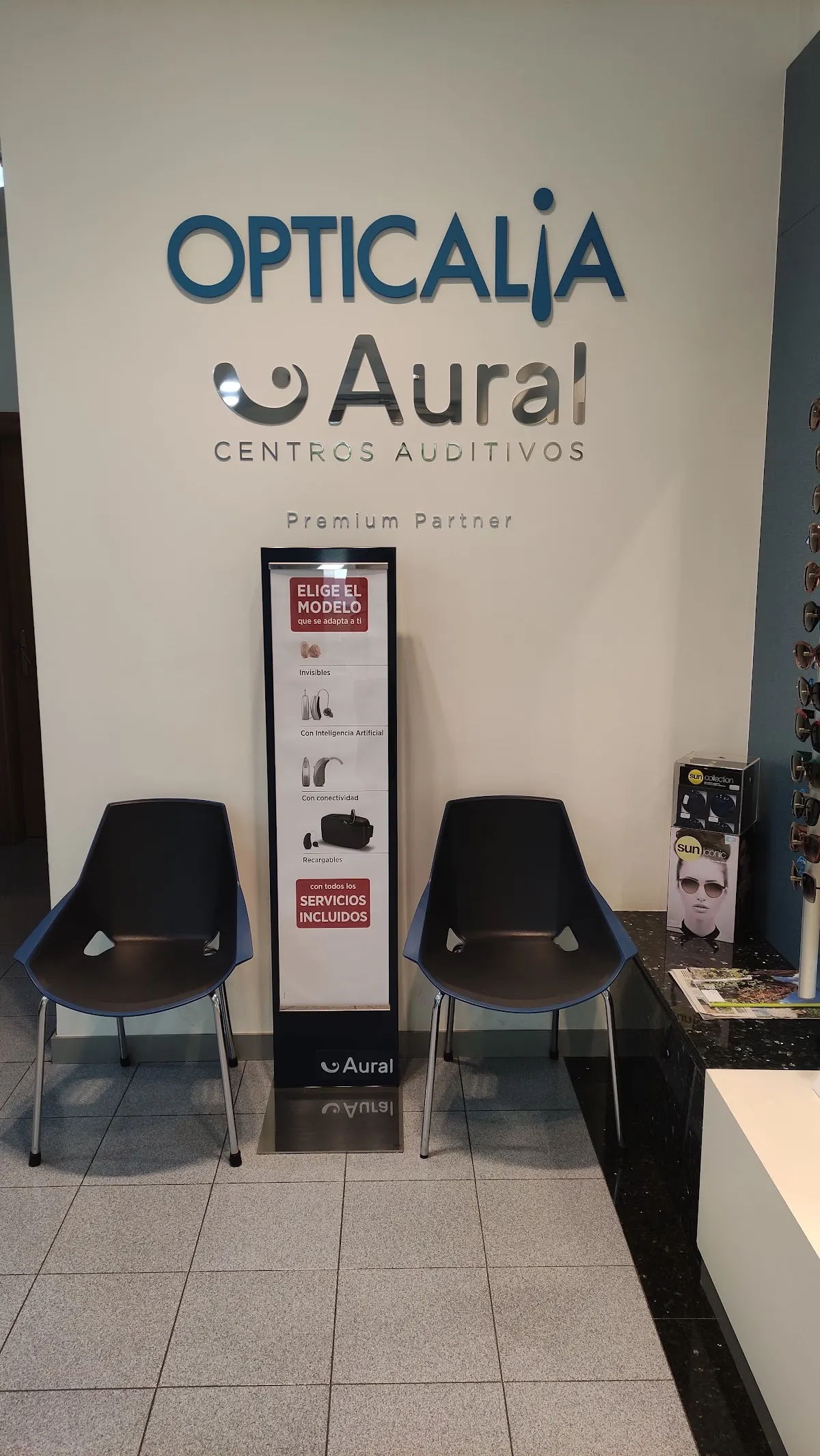 Zona de espera de Opticalia con dos sillas y un panel de centros auditivos.