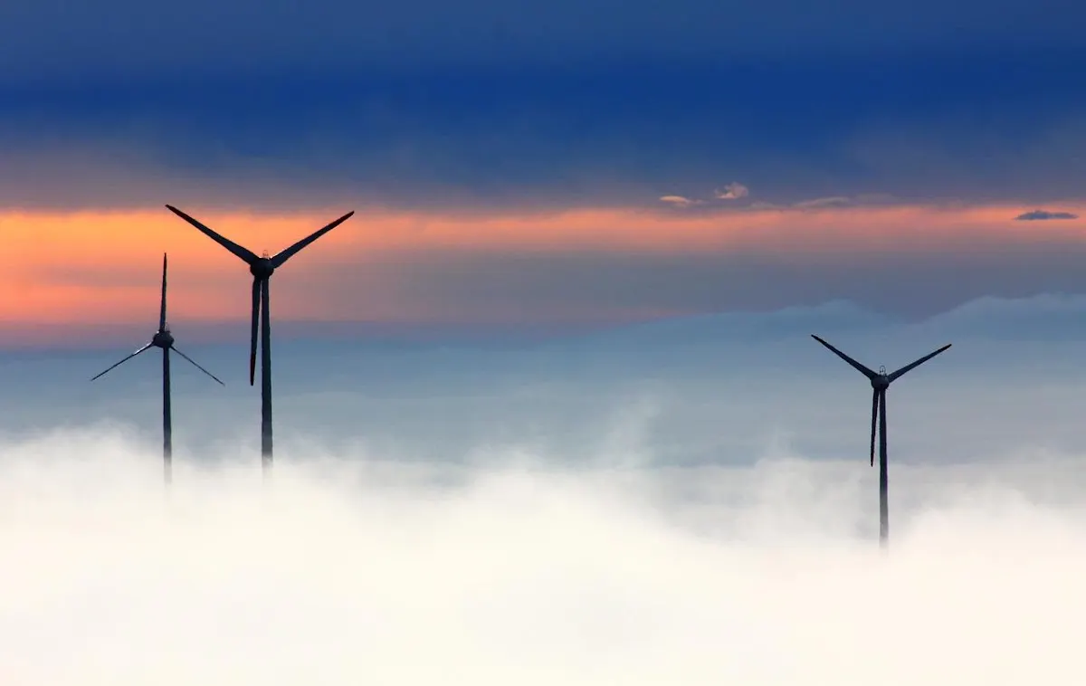 Tres aerogeneradores sobre un mar de nubes al atardecer.