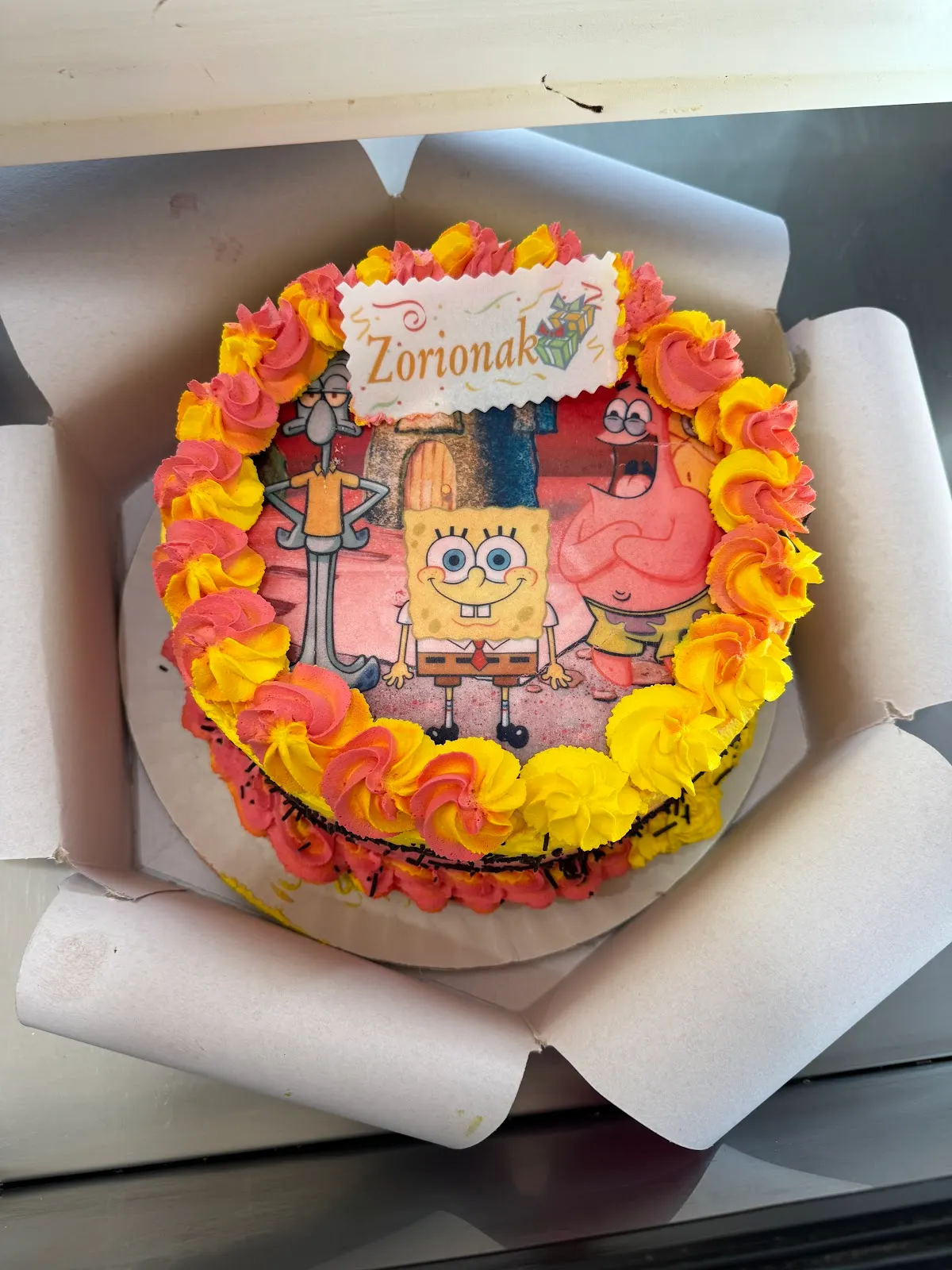 Tarta decorada con flores de crema e imagen de personajes de dibujos animados.