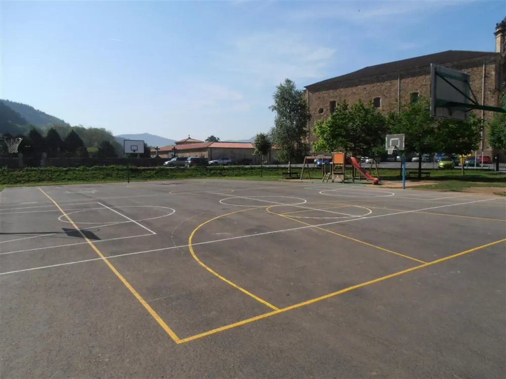 Pista exterior con canastas y juegos infantiles junto a la haurreskola.