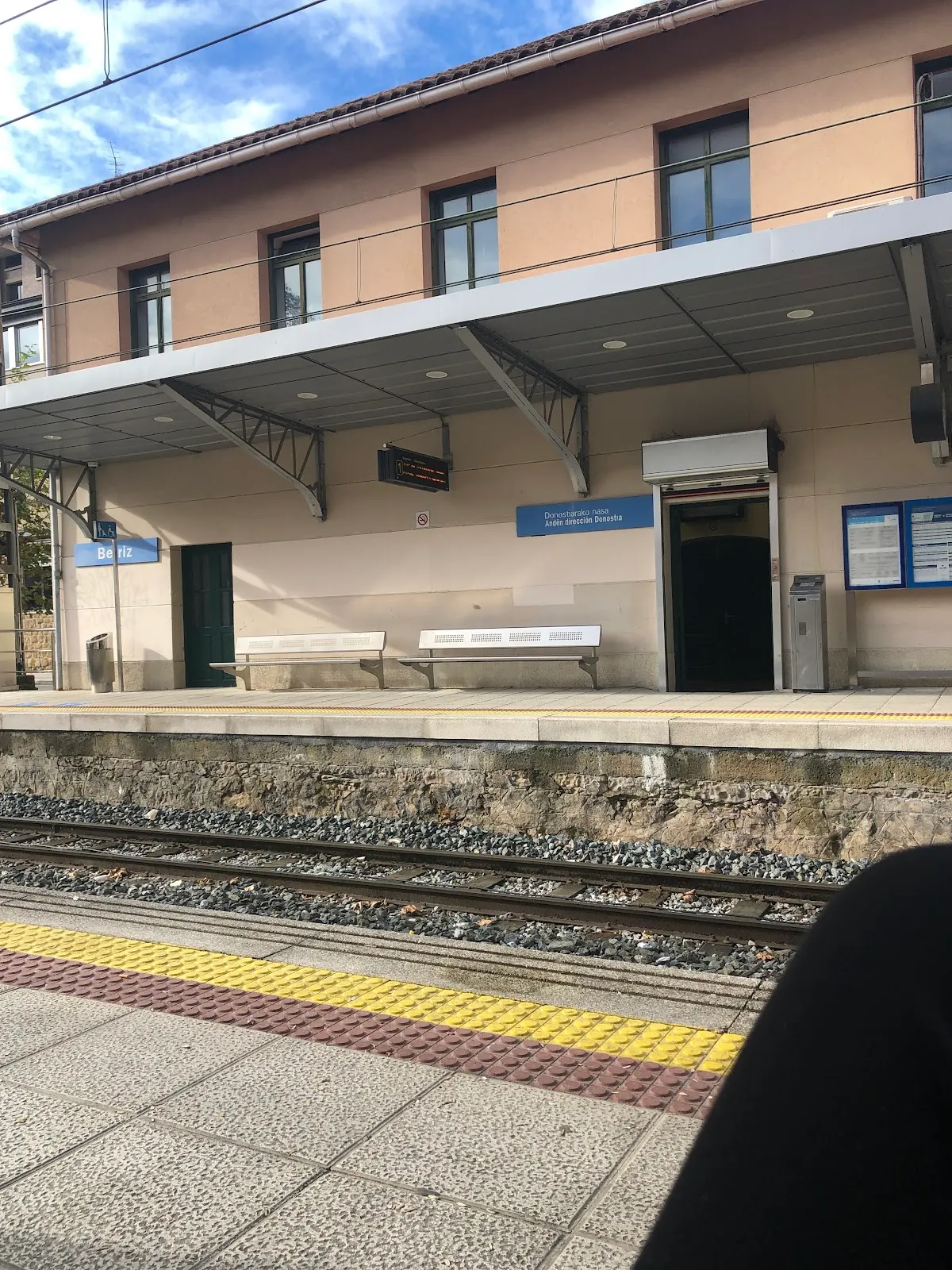 Andén de una estación ferroviaria con vías y bancos; no se identifica el negocio.