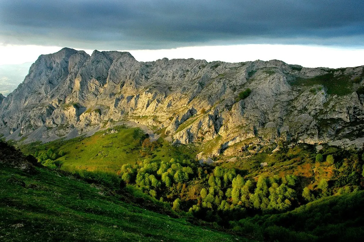 Paisaje de montaña con laderas verdes y una cresta rocosa.