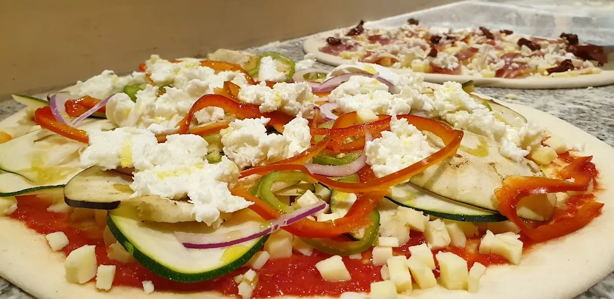 Pizza con verduras, queso y otros ingredientes antes de hornearse