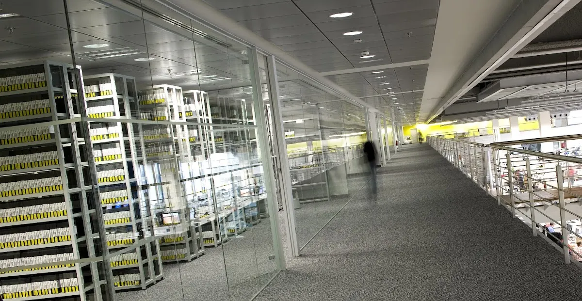 Pasillo de oficina con estanterías y divisiones de cristal.