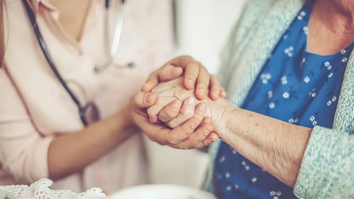 Profesional sanitaria acompaña y sostiene las manos de una persona mayor