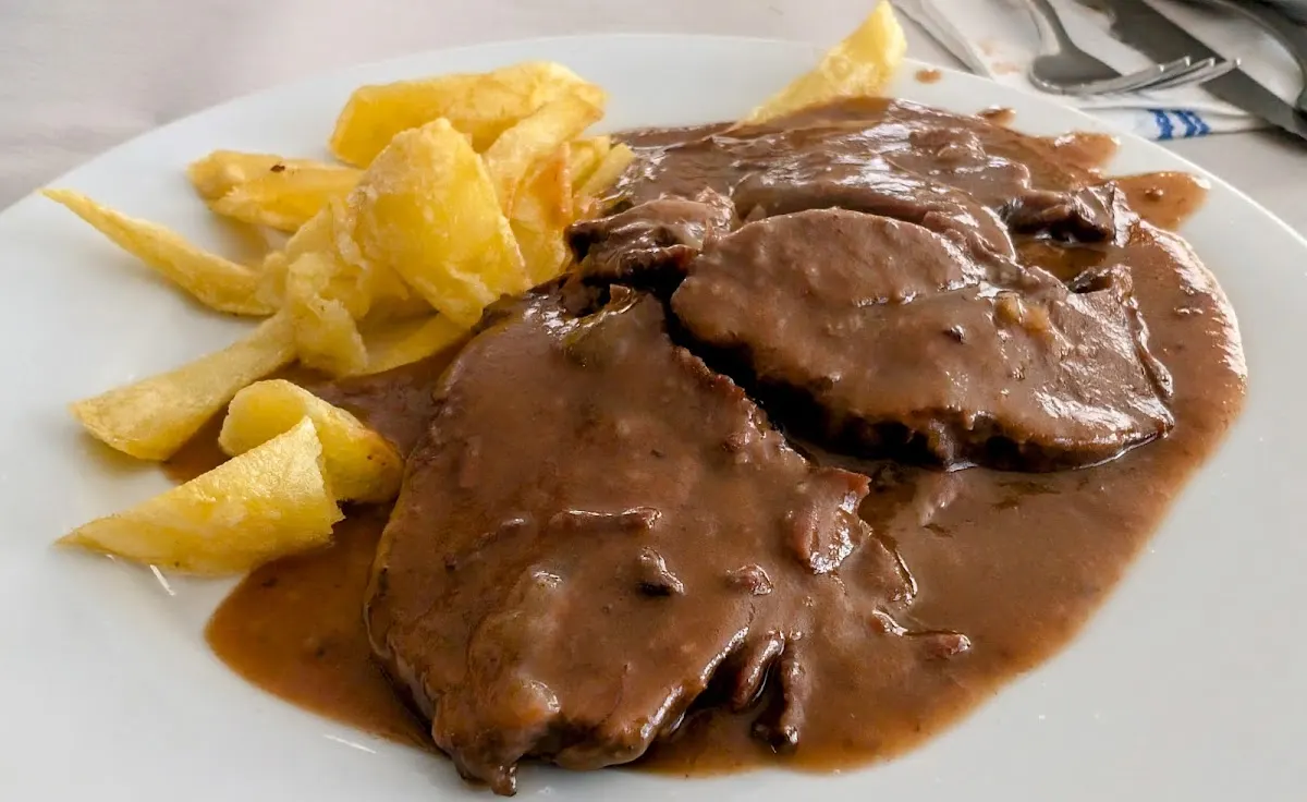 Plato de carne con salsa y patatas fritas.