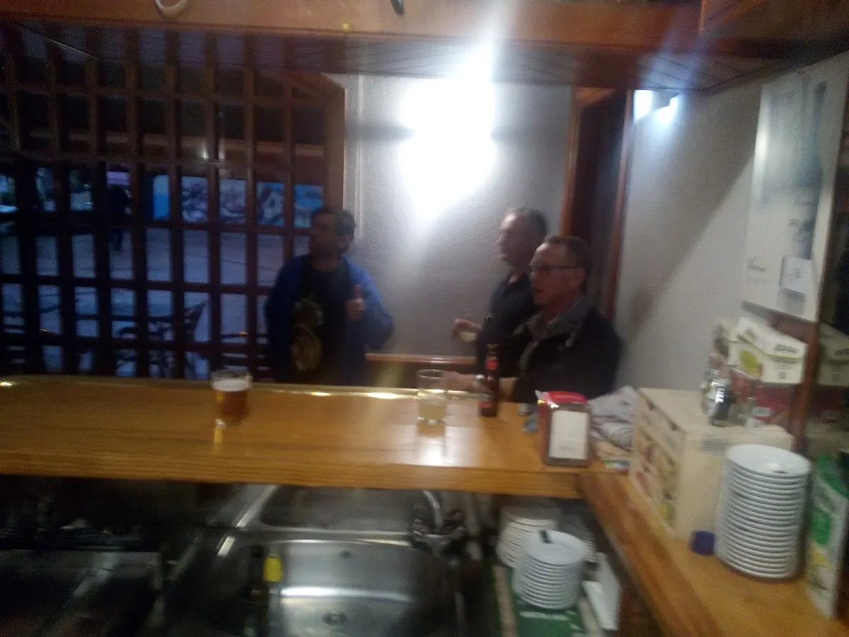 Interior de un bar con barra de madera, platos y varias personas.