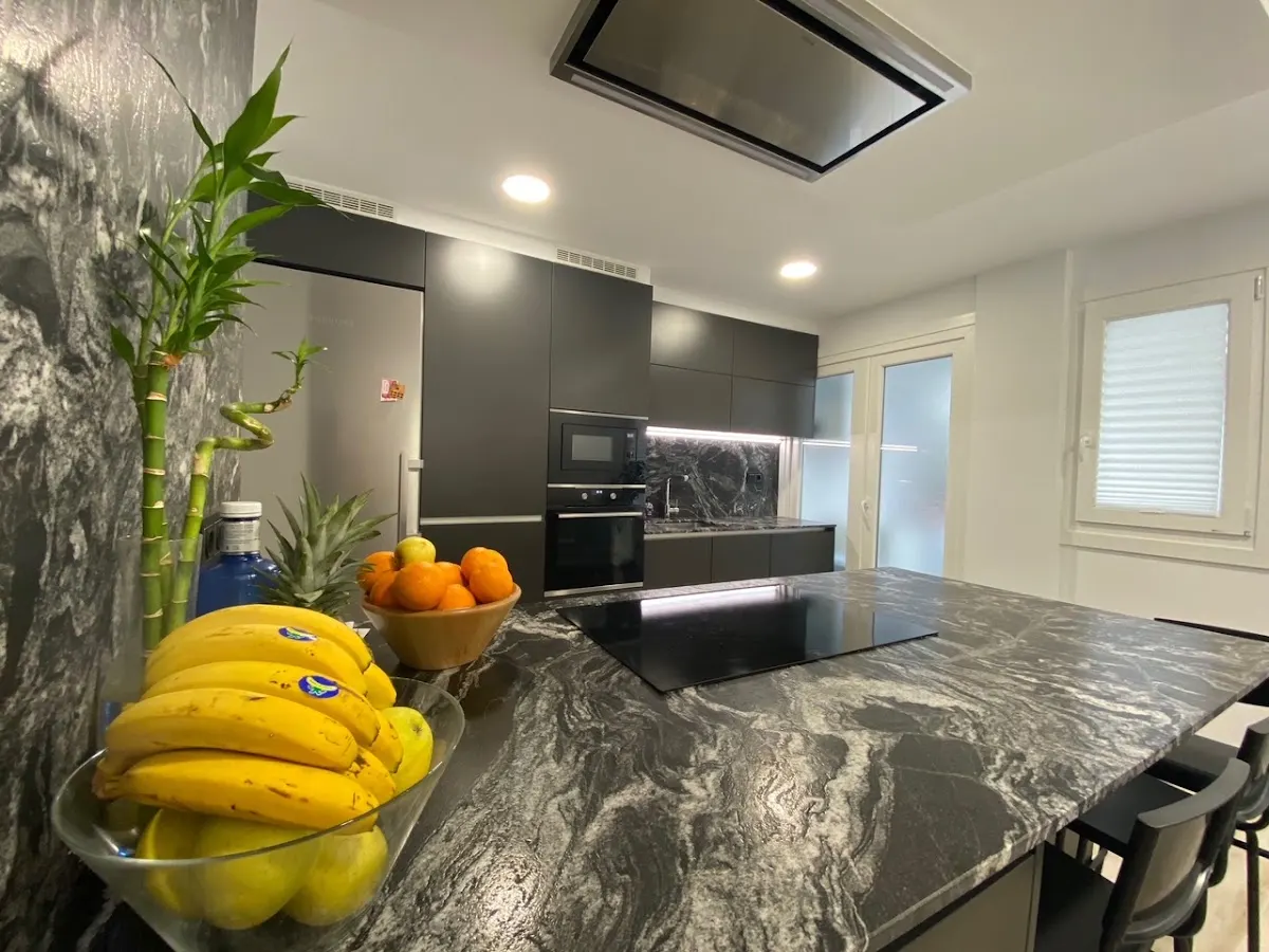 Cocina con muebles oscuros, encimera de piedra y electrodomésticos integrados.