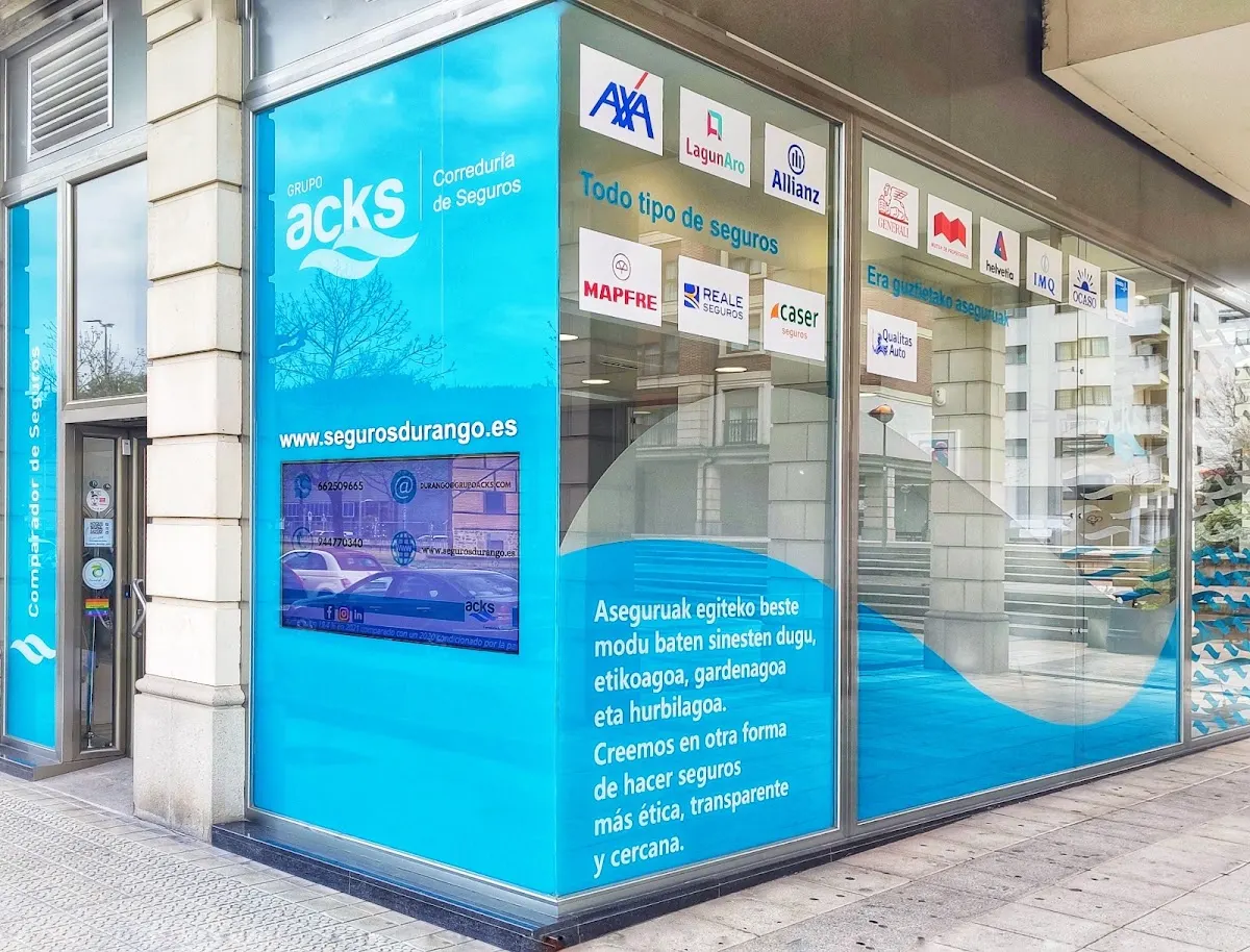 Fachada acristalada de Seguros Durango - Grupo ACKS en Durango, con rótulos de aseguradoras.