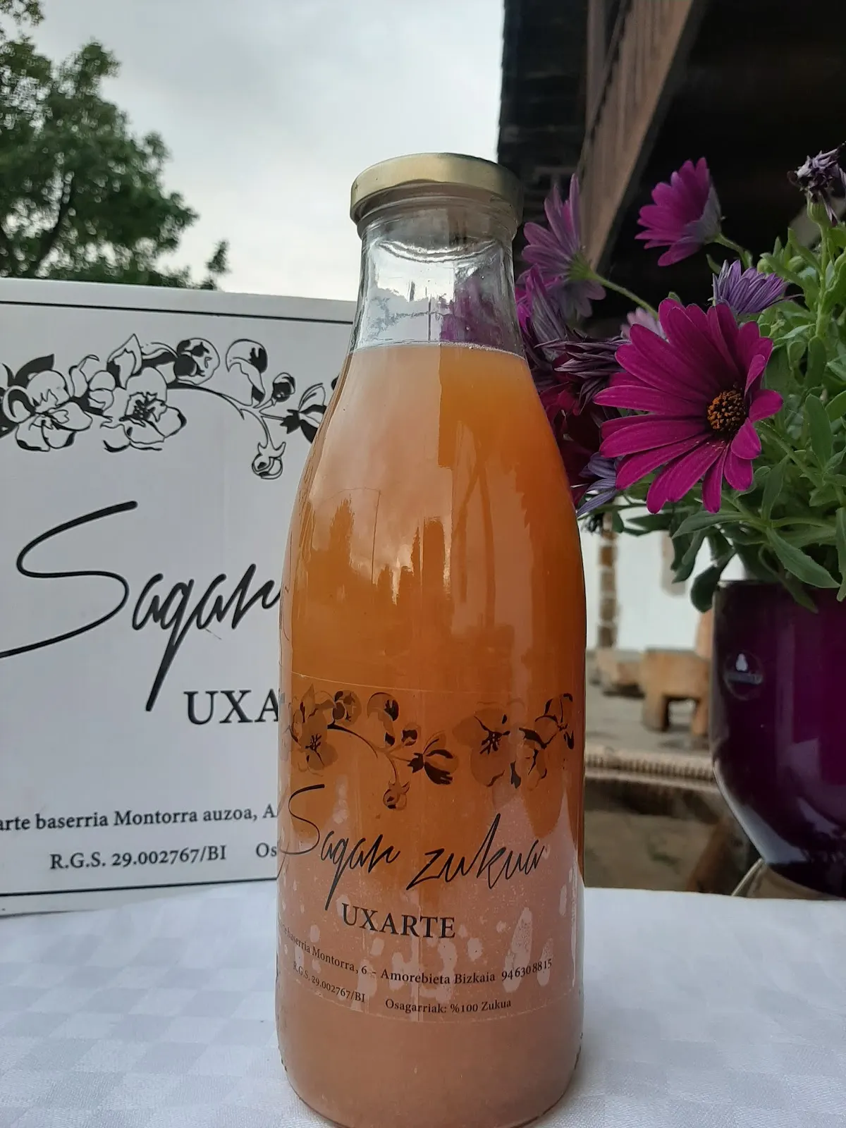 Botella de sidra Uxarte junto a flores y un cartel del establecimiento.