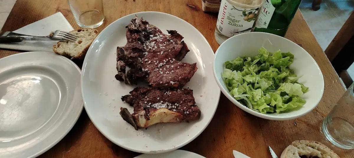 Chuleta a la parrilla y ensalada servidas en una mesa de Sidrería Uxarte.