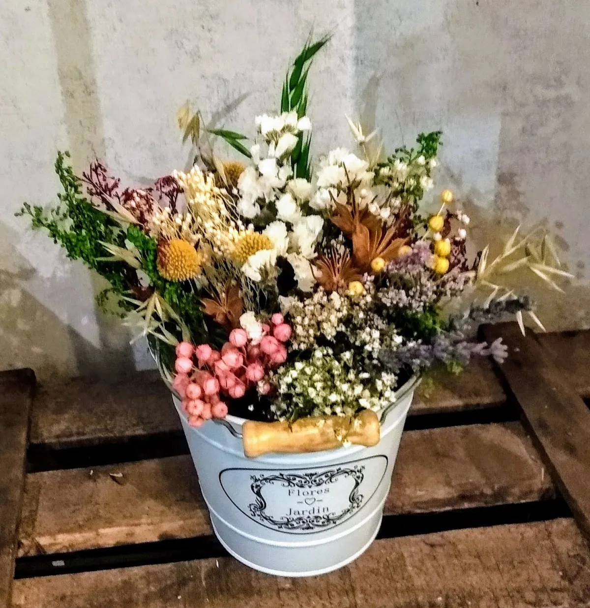 Centro floral de flores secas y preservadas en un recipiente decorativo.