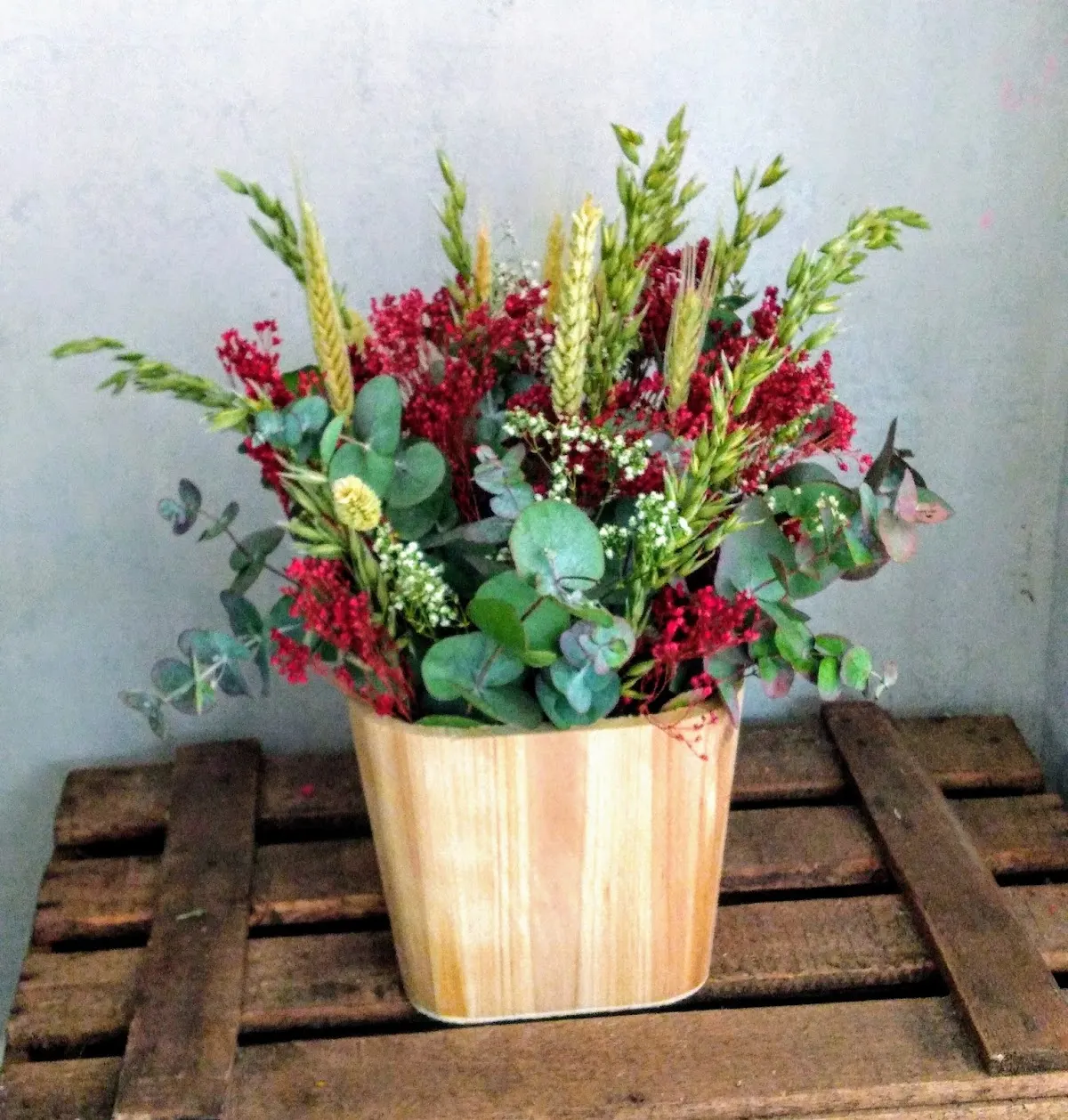 Arreglo floral con flores rojas, verdes y amarillas en un jarrón de madera.