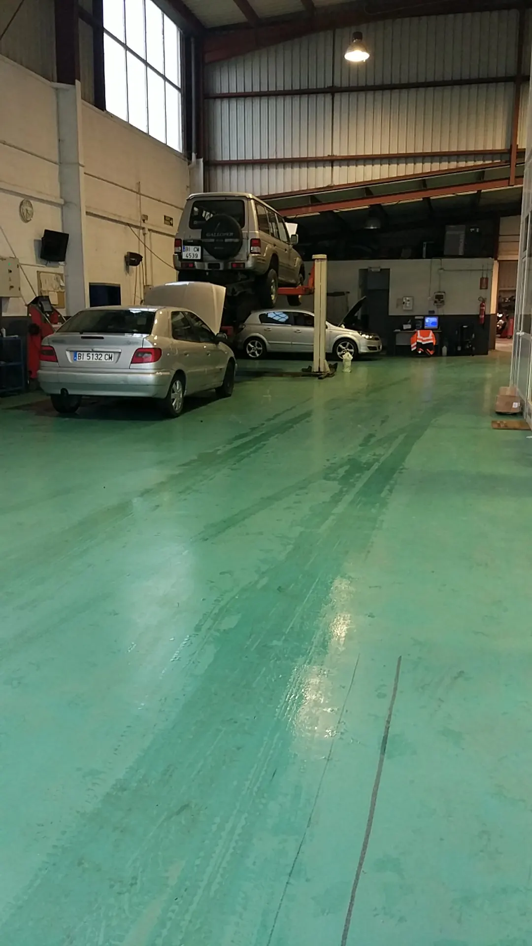 Interior del taller de TALLERES GARIZURIETA SL con coches en reparación y un vehículo elevado en un elevador.
