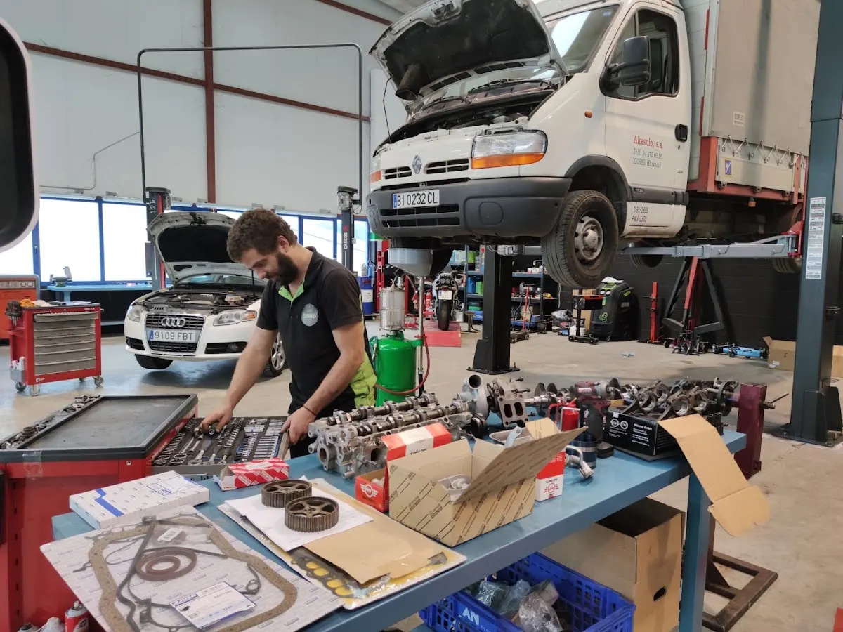 Mecánico de Talleres Solazaga trabajando en un taller con un vehículo industrial elevado y piezas sobre una mesa.