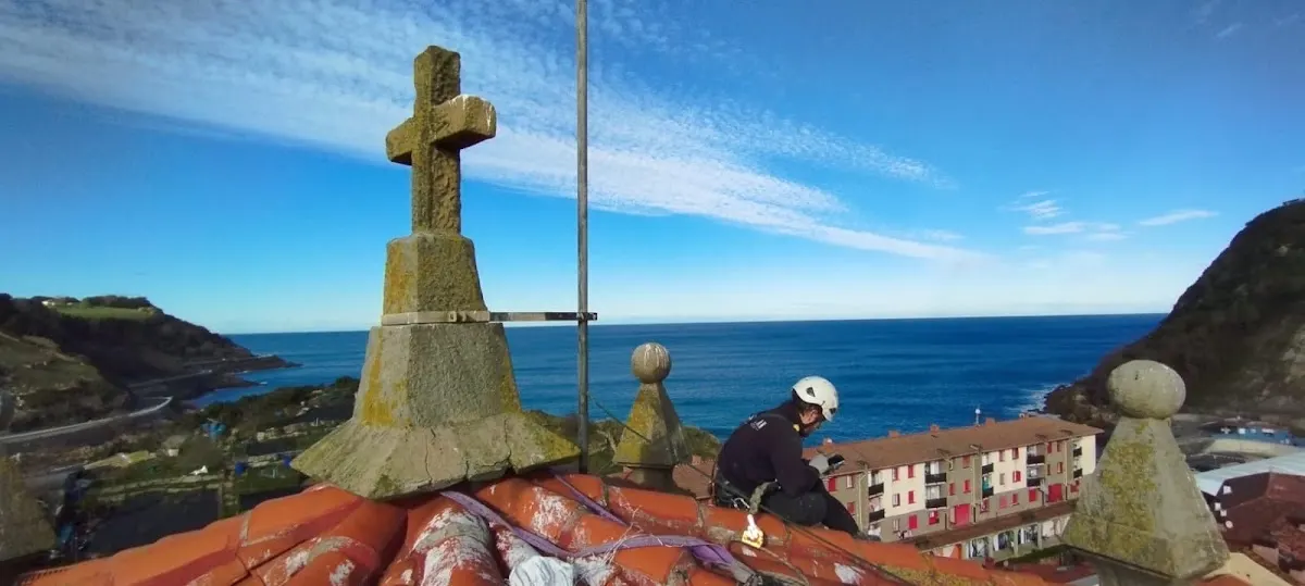Trabajador realizando trabajos verticales en un tejado con vistas al mar.