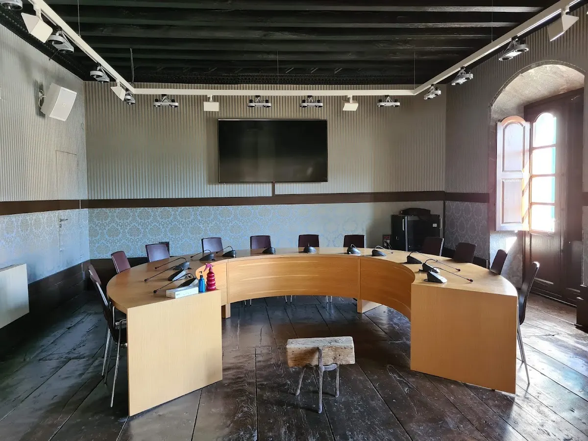 Sala interior con una mesa de reuniones en forma de U, sillas y una pantalla.