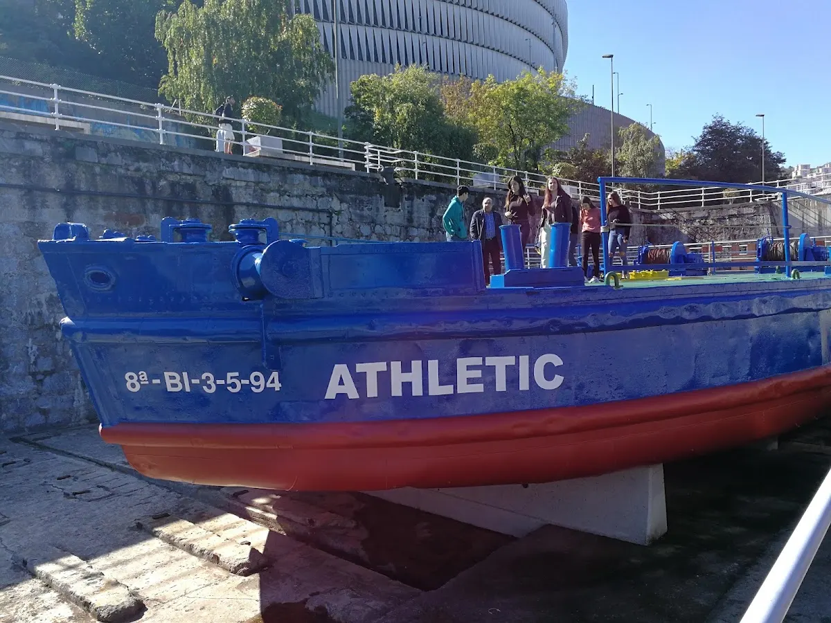 Barco azul del Athletic en tierra, junto a varias personas