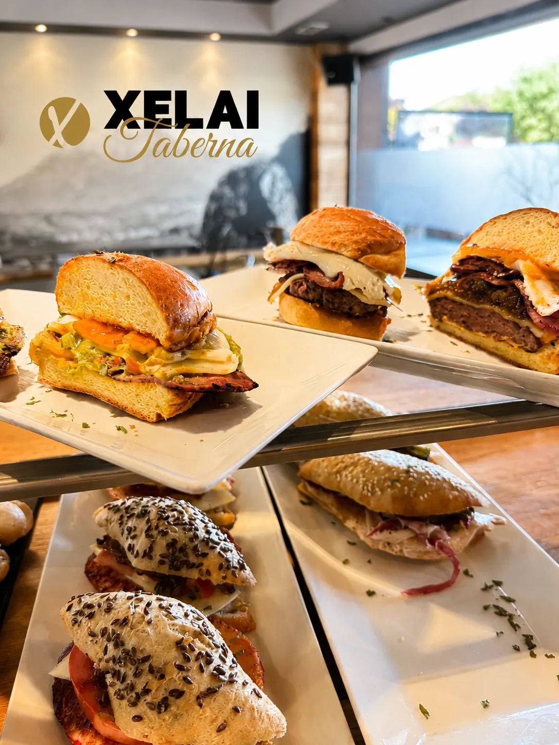 Varios bocadillos y sándwiches sobre una mesa, con el rótulo de Xelai Taberna al fondo.